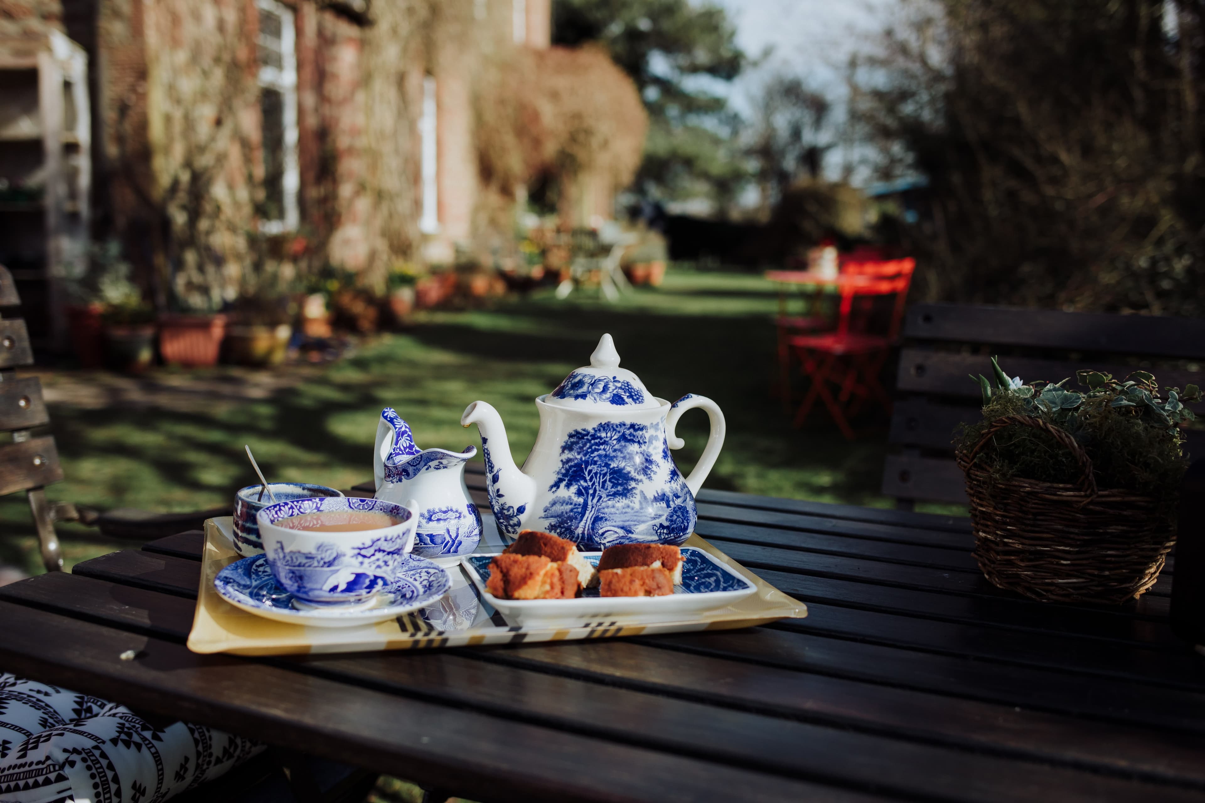 A teapot, some cups and a pastry presentation with the garden cafe in the background.